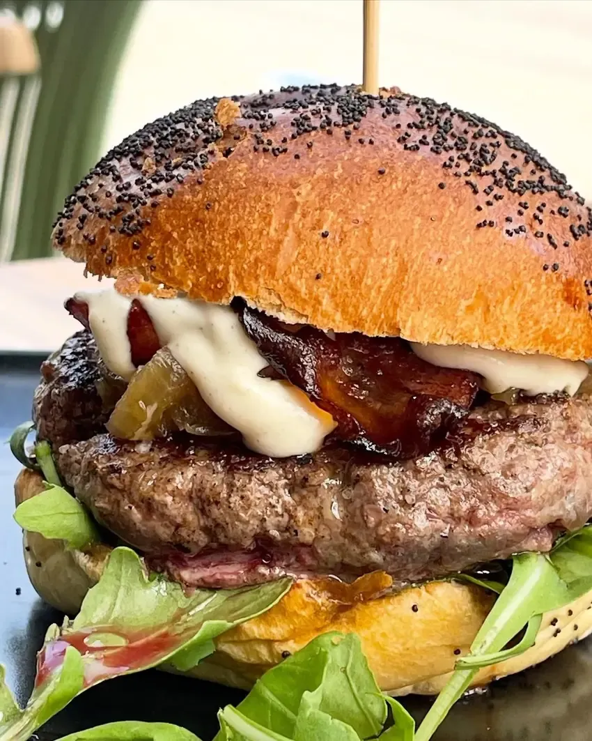 Hamburguesa en pan de amapola con bacon, queso fundido, jalapeños y rúcula
