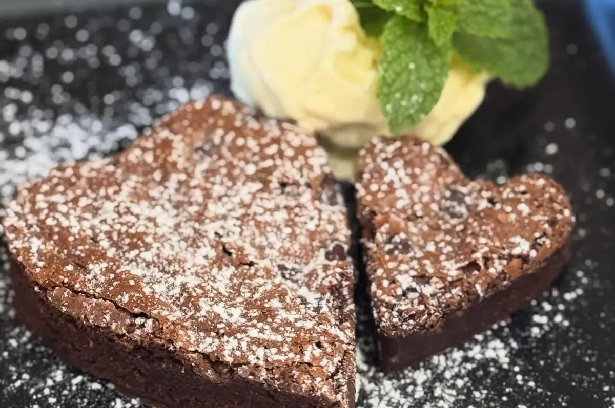 Brownie casero espolvoreado de azúcar glas con una bola de helado y menta fresca