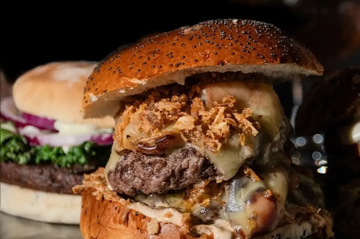 Hamburguesa con queso fundido, cebolla crujiente y encurtidos en pan brioche, servida en la barra