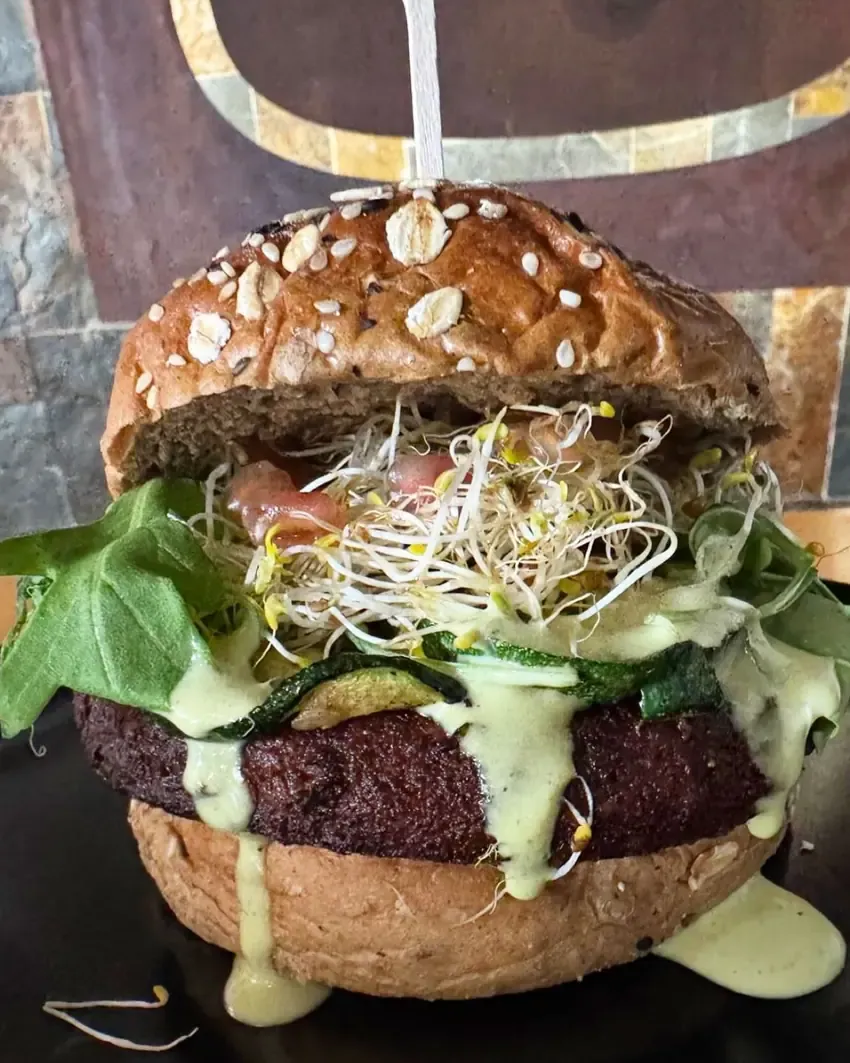 Hamburguesa vegetal en pan integral con brotes, calabacín y salsa verde