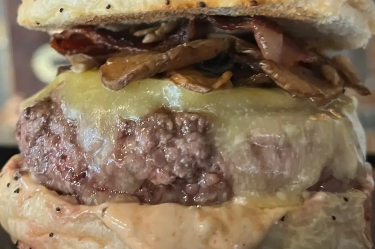 Hamburguesa coronada de champiñones salteados bajo una capa de queso fundido