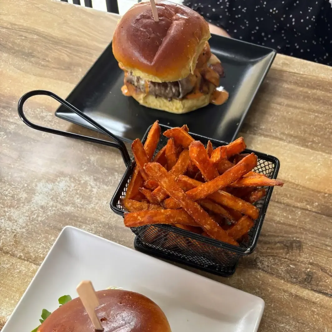 Mini hamburguesa sobre pizarra junto a un cestillo metálico de boniato en tiras