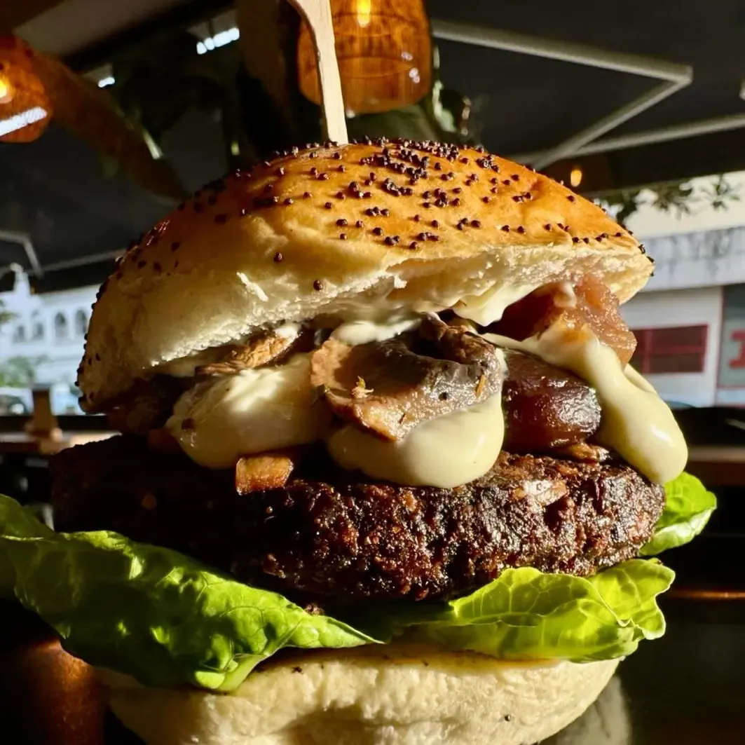 Hamburguesa vegetal alta con cebolla caramelizada, queso fundido y lechuga